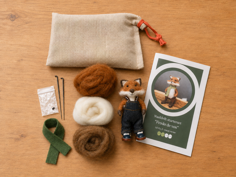 A felted wool kit arranged on a wooden surface, including a beige drawstring pouch, wool balls in brown, white, and green, two needles, a small plush fox figure in blue overalls, and an instruction card.